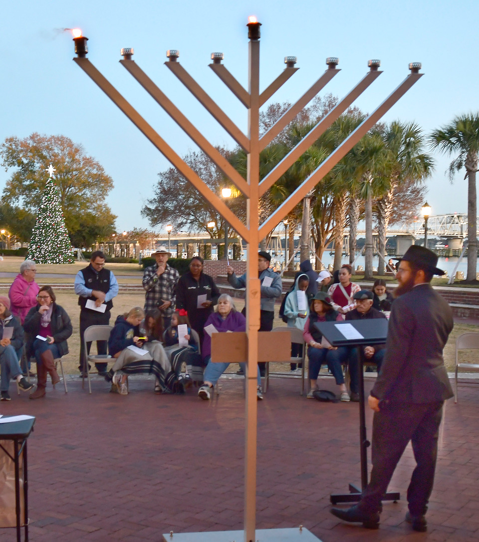 After lighting the menorah at the beginning of sunset Thursday, Dec. 7, Rabbi Mendel Hertz, right, discusses “light over darkness” to begins the eight days of the Jewish holiday of Hanukkah at Henry C. Chambers Waterfront Park. Each lamp of the menorah commemorates the Jewish victory over the Syrian armies in 164 BC. Following the war, there was only a tiny bit of oil for lamps for re-dedication of the Second Temple of Jerusalem. Miraculously, the lamp burned for eight days. Bob Sofaly/The Island News