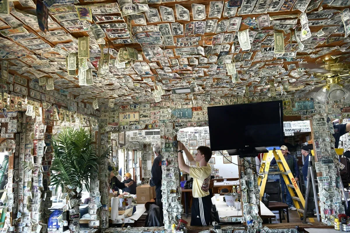 Money seems to be falling from the ceiling of Johnson Creek Tavern in 2020 as Craig Bowman, center, and volunteers remove thousands of dollar bills destined to be donated to charity. File photo by Bob Sofaly